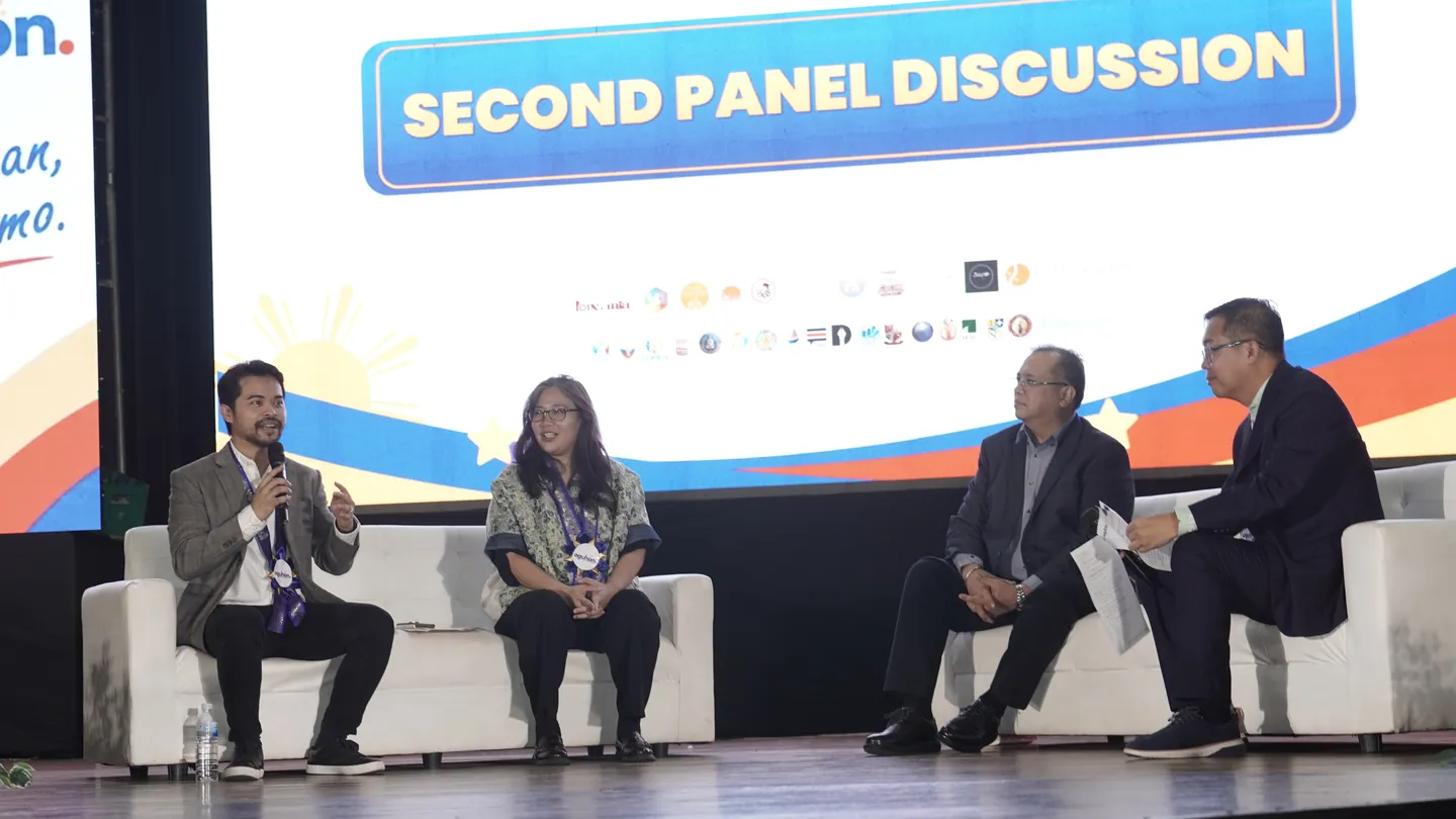 Atty. Third Bagro speaks into a microphone from a white sofa on stage, with three other panelists seated beside him under a screen reading “Second Panel Discussion”